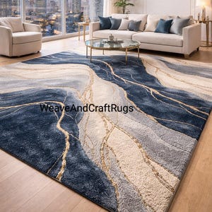 May include: A large rug featuring a flowing design in shades of blue, grey, and beige. Gold lines weave through the design, creating a marbled effect. The rug is placed on a wooden floor. The text "WeaveAndCraftRugs" is visible.