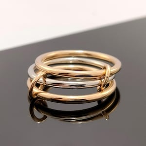 May include: Three interlocked rings, two gold and one silver, are displayed. The rings are smooth and polished, reflecting light. The gold rings have a warm, yellow tone, while the silver ring is a bright, cool colour. The rings are likely jewellery.