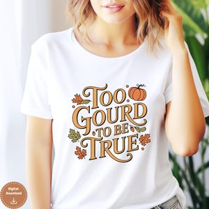 Peut inclure: T-shirt blanc avec l'inscription "Too Gourd to be True" en orange et vert, ornée d'une citrouille et de feuilles d'automne. Le t-shirt est à col rond et à manches courtes.