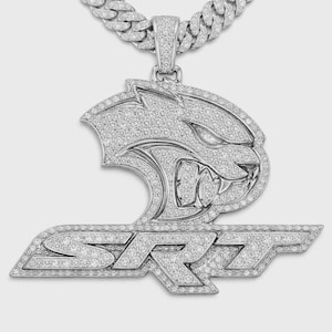 May include: A silver-toned pendant necklace featuring a detailed design of a snarling cat head above the letters SRT. The pendant and chain are encrusted with small, sparkling stones.