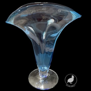 May include: A tall, light blue glass vase with a flared top and a round base. The vase has a unique, organic shape and is made of transparent glass. The vase is likely used for decorative purposes.