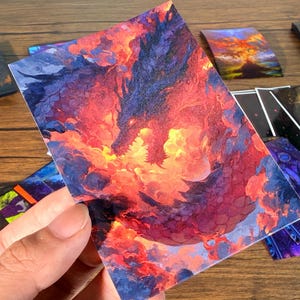 Pu&ograve; includere: Una collezione di carte d'arte fantasy con un drago nei toni infuocati del rosso, arancione e viola. Altre carte presentano disegni celesti e astratti. Le carte sono rettangolari e hanno una finitura lucida, adatte per collezionare o giocare.