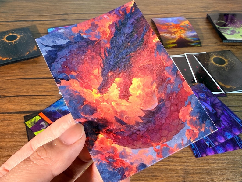Pu&ograve; includere: Una collezione di carte d'arte fantasy con un drago nei toni infuocati del rosso, arancione e viola. Altre carte presentano disegni celesti e astratti. Le carte sono rettangolari e hanno una finitura lucida, adatte per collezionare o giocare.