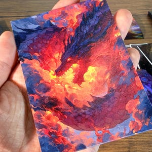 Pu&ograve; includere: Una carta artistica fantasy con un drago rosso e viola avvolto dalle fiamme. La testa del drago &egrave; visibile, con la bocca aperta, su uno sfondo infuocato. Altre carte con disegni simili sono visibili sullo sfondo.