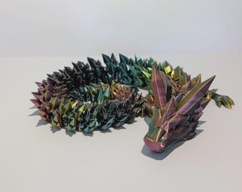 Könnte beinhalten: Eine 3D-gedruckte Drachenfigur mit kristallartigem Design. Der Drache ist in den Farbtönen Lila, Grün und Gold gehalten. Die Figur befindet sich auf einer weißen Oberfläche.