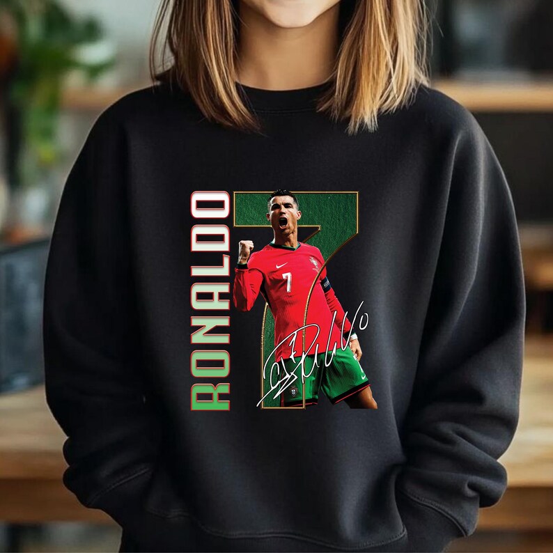 May include: Black sweatshirt featuring a graphic of a soccer player in a red jersey with the number 7. The image includes the player's signature and the name "RONALDO" in green and red.