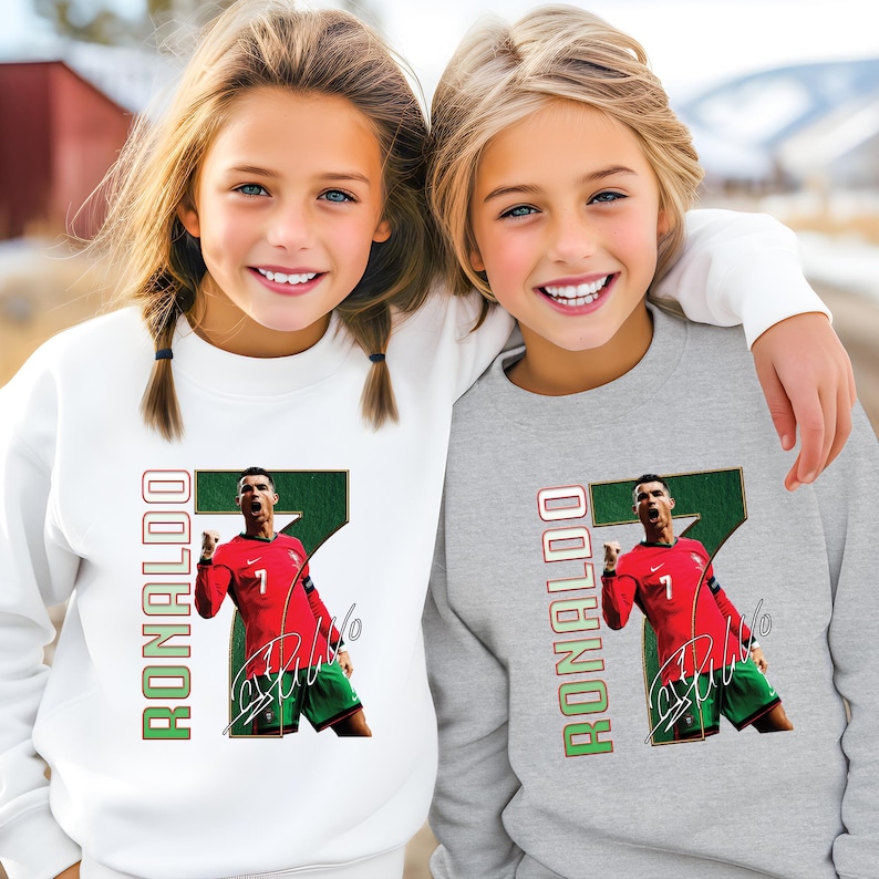 May include: Two children wearing white and gray sweatshirts. Each sweatshirt features a graphic of a soccer player in a red jersey with the number 7, green shorts, and the name "RONALDO" in green and red.