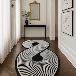 Op de afbeelding: Een zwart-wit patroon tapijt in een oneindigheidssymbool vorm. Het tapijt heeft een herhalend gestreept ontwerp en is geplaatst op een donkere houten vloer in een gang. Het tapijt is een decoratief woondecoratie-item.