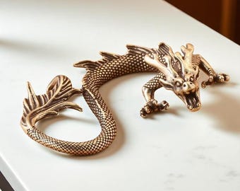 May include: A bronze-colored dragon figurine with intricate detailing. The dragon is posed in a curved shape, with its head and tail forming a circle. The dragon's scales, claws, and facial features are clearly defined, giving it a realistic appearance.