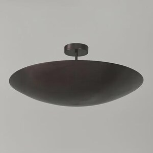 May include: A dark bronze-colored, modern ceiling light fixture. The light has a large, shallow, oval-shaped shade and a small, circular base that attaches to the ceiling. The fixture is suspended by a short, straight rod.