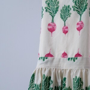 Puede incluir: Delantal blanco roto con un estampado repetido de r&aacute;banos rosas y hojas verdes. El delantal tiene un dobladillo con volantes y correas, ideal para la cocina o el jard&iacute;n. El dise&ntilde;o de r&aacute;bano a&ntilde;ade un toque de fantas&iacute;a.