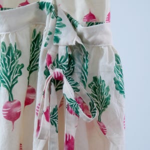 Puede incluir: Vestido cruzado blanco con un estampado de r&aacute;banos rosas y hojas verdes. El vestido tiene un cierre de lazo en la cintura y un dobladillo con volantes. La tela es ligera y adecuada para el verano.