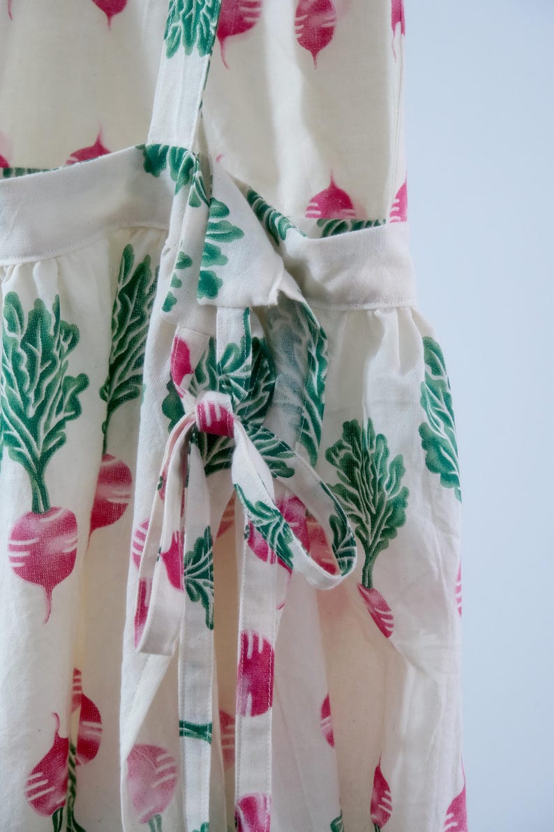Puede incluir: Vestido cruzado blanco con un estampado de r&aacute;banos rosas y hojas verdes. El vestido tiene un cierre de lazo en la cintura y un dobladillo con volantes. La tela es ligera y adecuada para el verano.