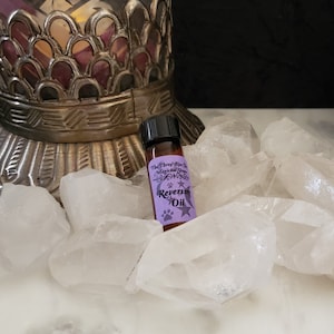 May include: A small brown glass bottle with a black cap, resting on a bed of white quartz crystals. The bottle label is purple and reads "The Three Wise Men Magical Supply" and "Reversing Oil" with a paw print and stars.