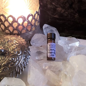 May include: A small brown glass bottle with a black cap, containing a clear liquid. The bottle has a white label with the text "The Three Wise Men Crystal Shop" and "Chakra Balancing Oil". The bottle is surrounded by clear quartz crystals.
