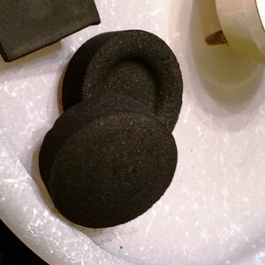 May include: Two round black charcoal briquettes for a hookah or shisha pipe.