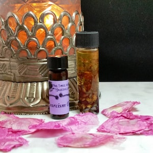 Può includere: Due piccoli flaconi di vetro con etichette viola e bianche. I flaconi contengono un liquido trasparente con piccole particelle che galleggiano al suo interno. I flaconi sono appoggiati su una superficie bianca con petali di fiori rosa sparsi intorno.