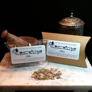 May include: A close-up of two small brown paper pouches with white labels that read "Purification Herbal Spell Mix". The pouches are filled with dried herbs and are sitting on a white surface. The text "The Three Wise Cats Magickal Shoppe" is printed on the labels.