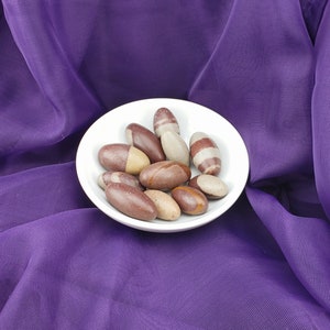 May include: A white ceramic bowl filled with brown and white striped stones. The bowl is sitting on a purple fabric background.