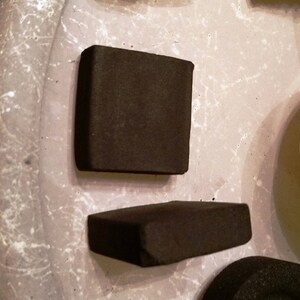 May include: Two rectangular black charcoal briquettes on a white surface.