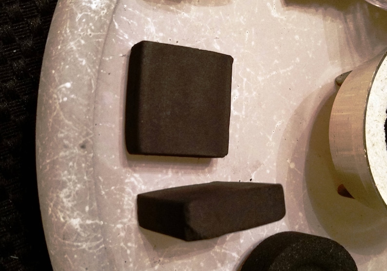 May include: Two rectangular black charcoal briquettes on a white surface.
