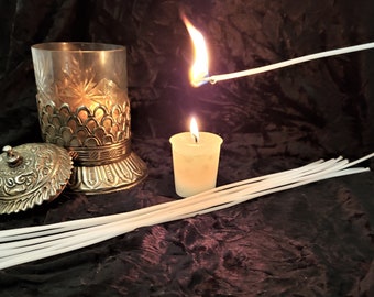 May include: A set of white candle wicks, a lit candle in a glass jar, and a lit tea light candle on a dark background.