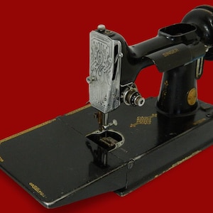 Peut inclure: Une machine à coudre Singer noire vintage dotée d'une plaque frontale en chrome brillant avec des motifs gravés complexes. Le corps de la machine est fini en émail noir brillant avec des décalcomanies décoratives dorées et un logo circulaire doré.