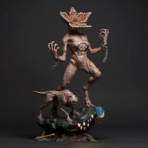 Könnte beinhalten: Detaillierte Skulptur einer Demogorgon-Kreatur aus der Serie Stranger Things, die auf einem felsigen Sockel mit einer kleineren Kreatur steht. Der Demogorgon hat einen blütenartigen Kopf und ist angekettet. Eine Baseballkappe und Lichterketten befinden sich auf dem Sockel.