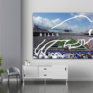 Può includere: Una grande stampa su tela raffigurante uno stadio di calcio affollato sotto un cielo blu. La parola "BILLS" è in bianco, con un contorno bianco di un bufalo sovrapposto al campo. Tema sportivo.