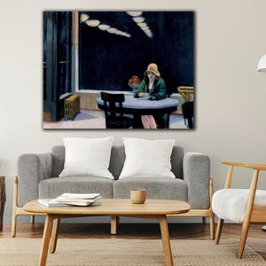 May include: A framed print of Edward Hopper's "Nighthawks" painting. The artwork depicts a woman in a green coat and hat seated at a table in a diner. The scene is set at night, with a dark background and bright lights.