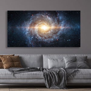 Peut inclure: Une grande impression sur toile rectangulaire représentant une galaxie vibrante. L'œuvre présente une spirale tourbillonnante de bleus, d'ors et de rouges, avec un cœur central brillant. L'impression est affichée au-dessus d'un canapé gris.