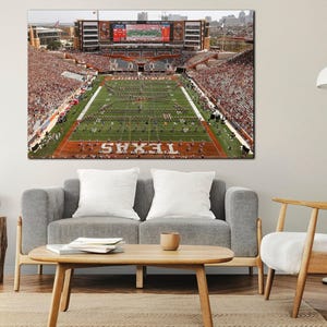 May include: A large canvas print of a football stadium filled with spectators. The field is green with white yard lines and the word "TEXAS" in large white letters. The stands are packed with fans wearing orange and white.