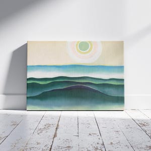 May include: An abstract landscape painting featuring rolling green hills under a pale yellow sky with a circular sun design. The artwork is displayed against a white wall and rests on a distressed, white-painted wooden floor.