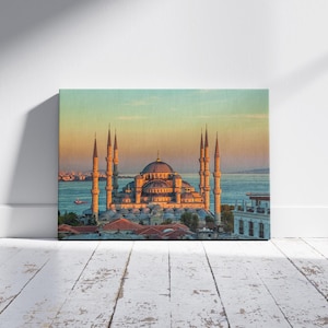 May include: A canvas print of the Blue Mosque in Istanbul, Turkey, at sunset. The image features the mosque's multiple minarets and domes, with the Bosphorus Strait in the background. The sky transitions from blue to orange.