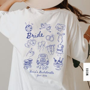 Könnte beinhalten: Weißes T-Shirt mit blauem Aufdruck auf dem Rücken. Das Design zeigt das Wort "Bride", eine Discokugel, Tauben, Ringe, einen Kuchen und ein Auto mit "Just Married". Der Text "Anna's Bachelorette Juni 2026" ist ebenfalls enthalten.