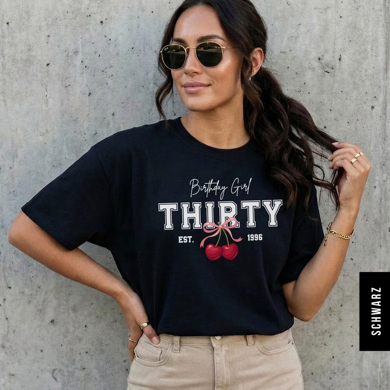 May include: A black short-sleeved t-shirt featuring the white text Birthday Girl THIRTY and EST. 1996. Below the text is a graphic of two red cherries tied together with a light pink ribbon. The shirt has a crew neckline and a standard fit.