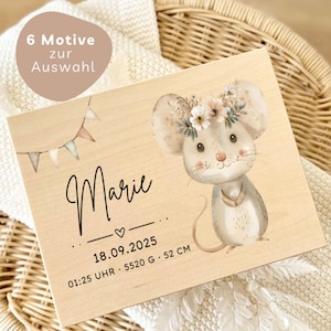 May include: A wooden plaque featuring a watercolor illustration of a mouse wearing a floral crown. The name "Marie" is written in cursive, along with birth details: date, time, weight (5520 g), and height (52 cm). A banner reads "6 Motive zur Auswahl".