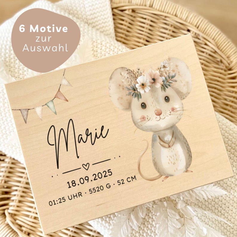 May include: A wooden plaque featuring a watercolor illustration of a mouse wearing a floral crown. The name "Marie" is written in cursive, along with birth details: date, time, weight (5520 g), and height (52 cm). A banner reads "6 Motive zur Auswahl".