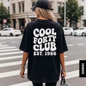 Pu&ograve; includere: Una t-shirt nera oversize con la scritta bianca COOL FORTY CLUB EST. 1986 sul retro in un carattere audace e ondulato. La maglietta ha maniche corte e una vestibilit&agrave; ampia, abbinata a un cappellino da baseball nero.