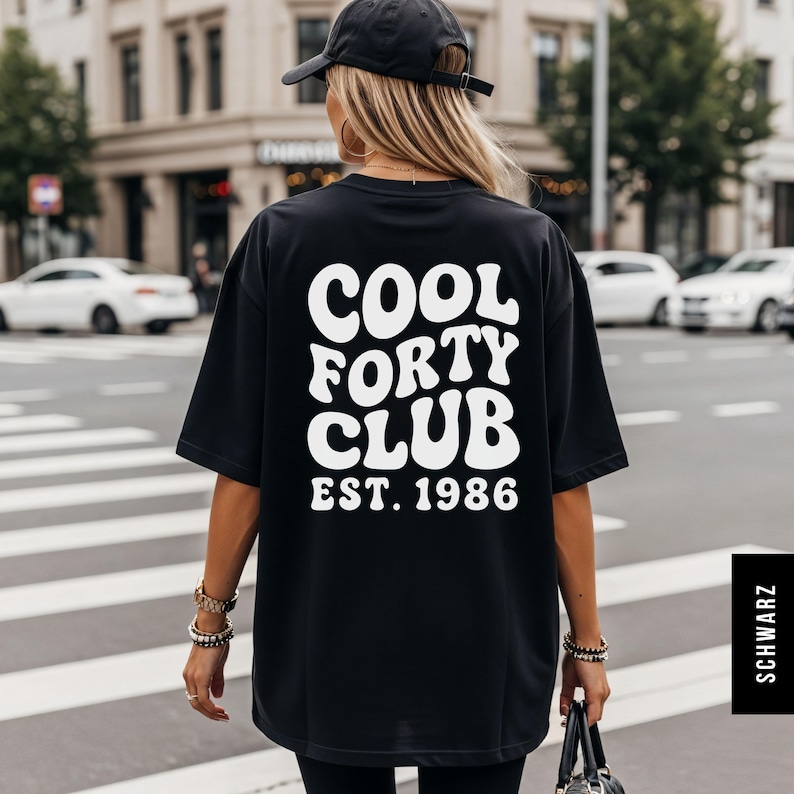 Pu&ograve; includere: Una t-shirt nera oversize con la scritta bianca COOL FORTY CLUB EST. 1986 sul retro in un carattere audace e ondulato. La maglietta ha maniche corte e una vestibilit&agrave; ampia, abbinata a un cappellino da baseball nero.
