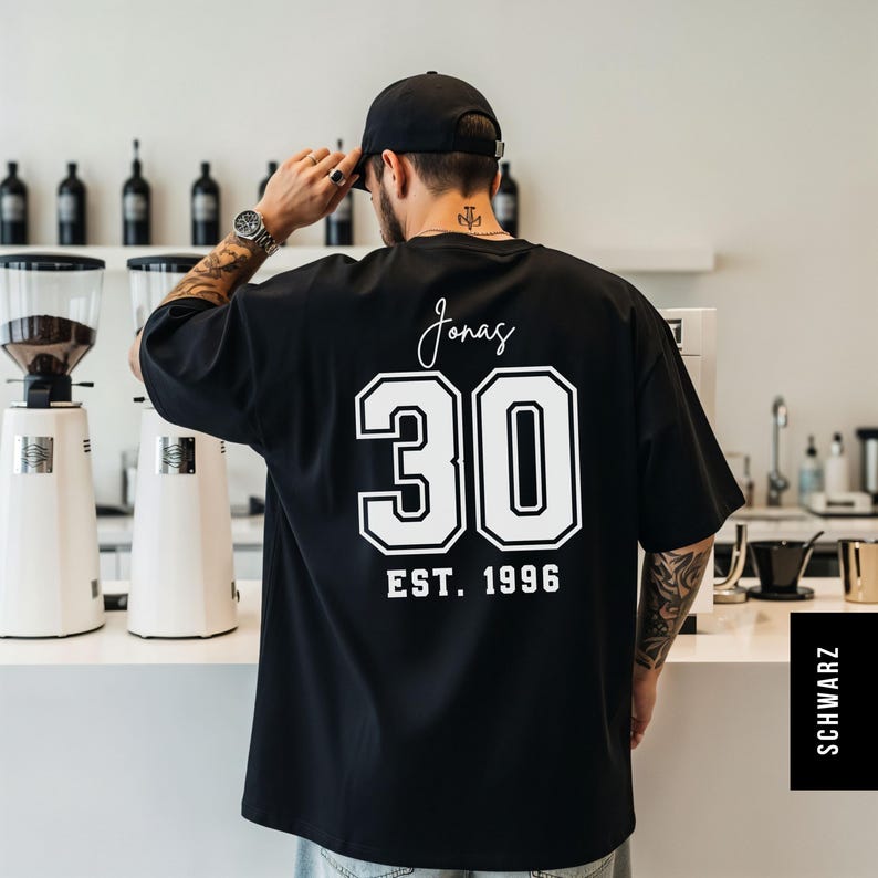 Op de afbeelding: Zwart oversized T-shirt met witte letters en cijfers. De achterkant van het shirt heeft de naam "Jonas", het nummer "30" en "EST. 1996". Het shirt heeft een casual stijl.