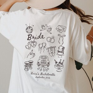 Könnte beinhalten: Ein weißes T-Shirt mit einer schwarzen Strichgrafik auf der Rückseite. Das Design zeigt eine Discokugel, Tauben, einen Umschlag, Ringe, eine Schleife, Herzmedaillons, Luftballons, Schuhe, Torte, Hand mit Ring, Auto mit Just Married Schild und Champagner. Text: Bride, Anna's Bachelorette, September 2026.