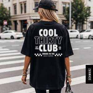 May include: A black short-sleeved t-shirt featuring white text on the back that reads COOL THIRTY CLUB, EST 1996, LVL 30, and CHEERS TO THE NEXT LEVEL, accompanied by a checkered pattern graphic. The shirt is worn with a black baseball cap.
