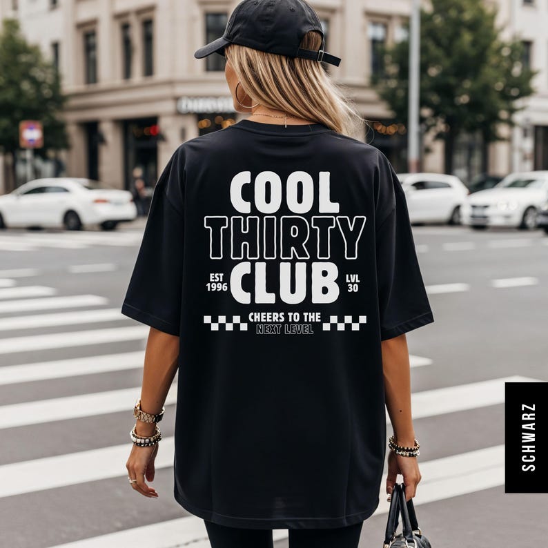 May include: A black short-sleeved t-shirt featuring white text on the back that reads COOL THIRTY CLUB, EST 1996, LVL 30, and CHEERS TO THE NEXT LEVEL, accompanied by a checkered pattern graphic. The shirt is worn with a black baseball cap.