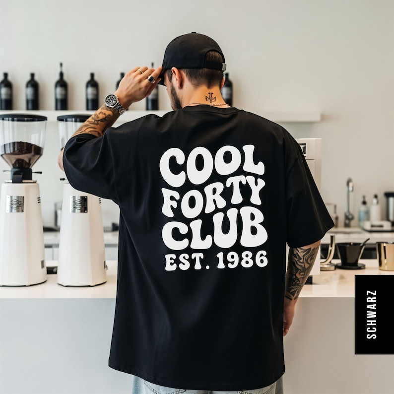 Pu&ograve; includere: Una t-shirt nera a maniche corte con la scritta bianca COOL FORTY CLUB EST. 1986 sul retro in un carattere ondulato e in grassetto. La maglietta ha una vestibilit&agrave; ampia e rilassata ed &egrave; indossata con un cappellino da baseball nero tinta unita.