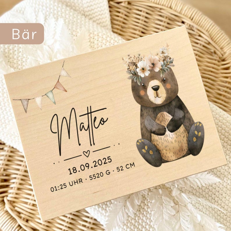 May include: A wooden plaque featuring a watercolor illustration of a bear wearing a floral crown. The plaque includes the name "Matteo", birthdate, time, weight (5520 grams), and length (52 cm). A small banner with pastel flags is also present.