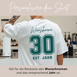 Op de afbeelding: Wit T-shirt met een groen en wit nummer 30 ontwerp op de achterkant. De tekst "Wunschname" staat boven het nummer en "EST. JAHR" eronder. Het shirt heeft ook de tekst "Personalisiere dein Shirt" bovenaan.