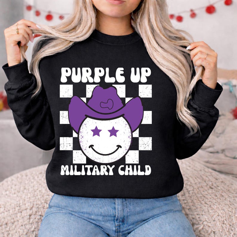 Puede incluir: Sudadera negra con el texto "PURPLE UP MILITARY CHILD". El dise&ntilde;o presenta una carita sonriente con un sombrero de vaquero morado con dos ojos de estrella, sobre un fondo a cuadros blanco y negro.