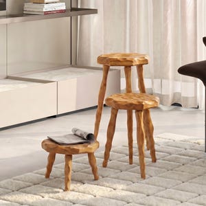 May include: Three light brown wooden stools with textured, uneven surfaces and rounded tops. The stools feature three legs each, with varying heights including one low stool, one medium stool, and one tall stool, all crafted from natural wood.