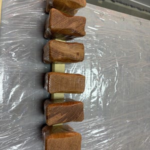 Puede incluir: Disposici&oacute;n vertical de seis bloques de madera tallada, cada uno con una superficie texturizada &uacute;nica y un tono marr&oacute;n c&aacute;lido. Los bloques est&aacute;n unidos a un soporte de madera de color claro, creando una est&eacute;tica r&uacute;stica y artesanal.